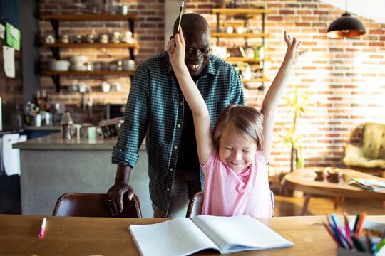Child celebrating homework success with mentor in home kitchen