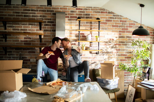 Happy couple eating pizza and taking a selfie while moving into a new apartment kitchen