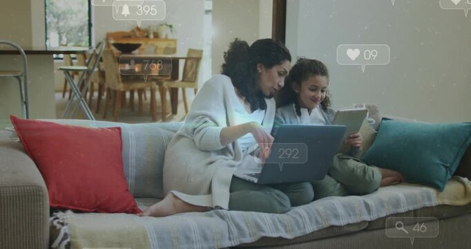 Mother with laptop watching social icons appearing, leaning and pointing tablet, guiding daughter