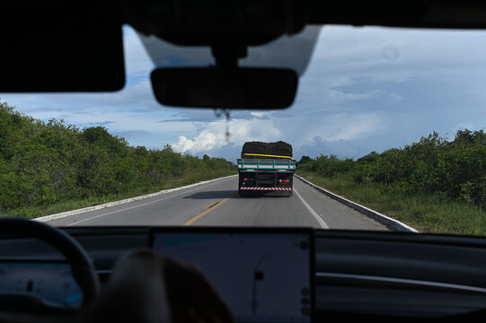 view from inside car following cargo truck on highway, driver point of view with gps navigation display, car interior perspective of road trip and logistics, steering wheel and windshield view of truc