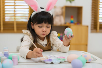 preschool child girl wearing bunny ears painting and decorating colorful egg at home on easter day