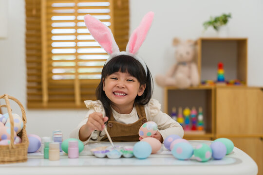 happy preschool child girl wearing bunny ears painting and decorating colorful egg at home on easter day