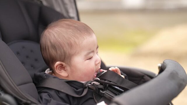 Man holds baby gently in park setting. Child smiles softly, eyes wide with wonder. Bright yellow tent stands behind bare trees. Distant pine tree adds depth to natural backdrop. Sunlight warms scene