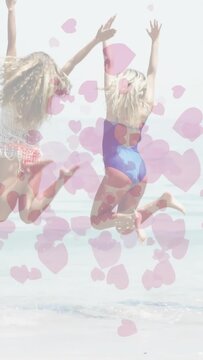 Two women entering surf raising arms then leaping and splashing bonding hearts overlaying marketing