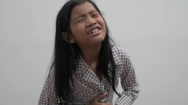 Little Asian girl feeling stomach ache and holding her belly with painful expression, child suffering from indigestion or stomach cramp, childhood illness and healthcare