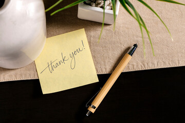 Thank you message on yellow sticky note with pen on desk, gratitude and appreciation concept.