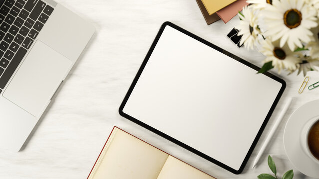 Top view white screen tablet and stylus with book and coffee aside flower and laptop on marble table