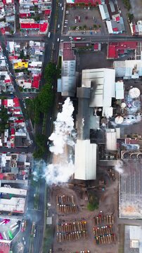 Industrial sugar mill emitting smoke from its chimneys next to a city with busy traffic