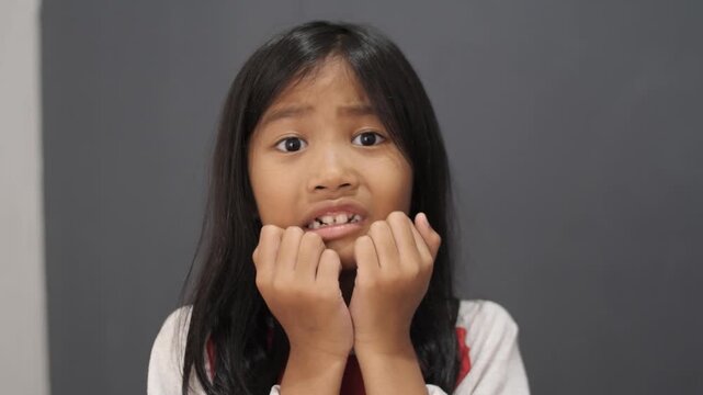 Anxious little Asian girl looking scared and worried, stressed child biting fingers with fearful expression, concept of childhood anxiety, bullying