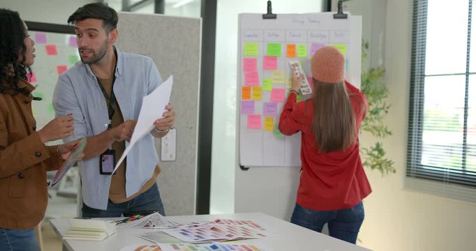 Diverse group of startup team engaging in brainstorming session, using sticky notes on glass wall to organize ideas, plan next steps. Creativity and collaborative spirit of modern entrepreneurial team