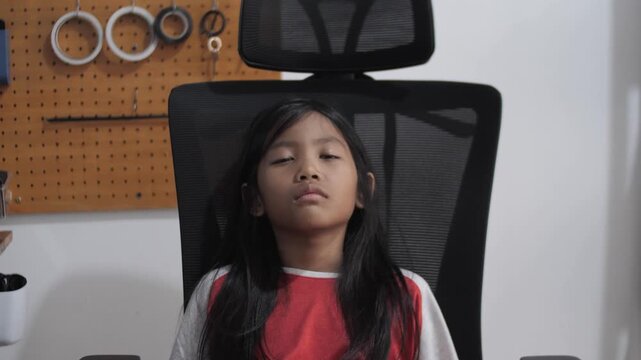 Tired little Asian girl sleeping on office chair, exhausted child napping after study, burnout, fatigue, and education stress