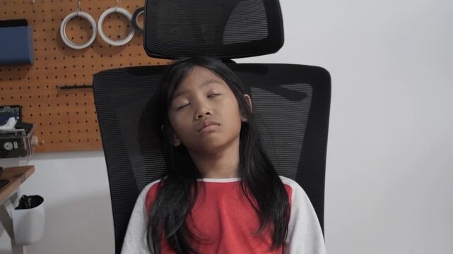 Tired little Asian girl sleeping on office chair, exhausted child napping after study, burnout, fatigue, and education stress