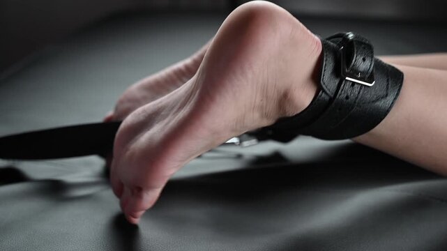 Women's legs in leather shackles. BDSM fetish.