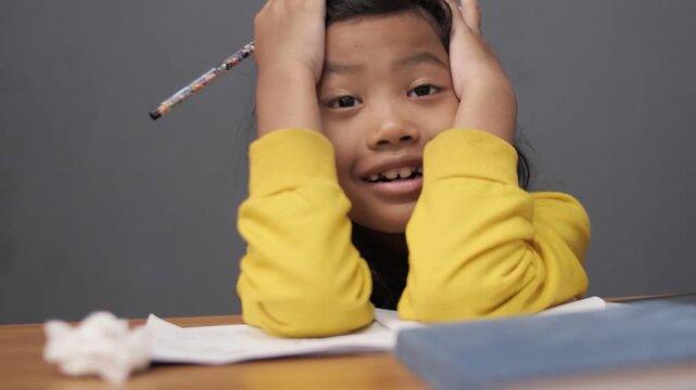 Stressed little Asian girl crying while studying, unhappy child having headache or difficulty with homework, academic pressure and learning disability