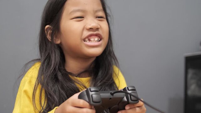 Extremely excited little Asian girl cheering while playing video games, joyful child shouting with happiness holding a controller, victory and gaming euphoria