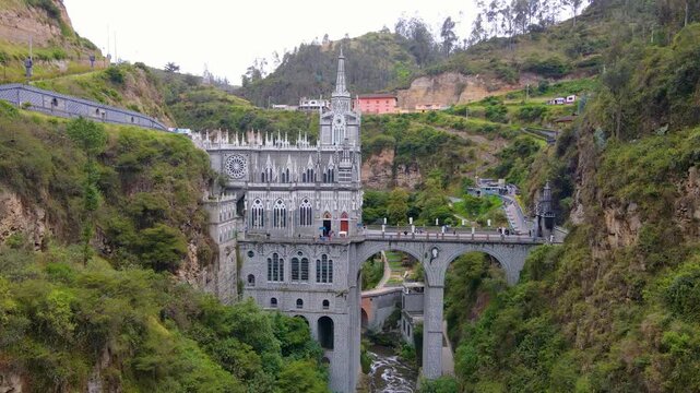 Aerial view of Las Lajas church with gothic stone facade and tall spire, spanning a stone bridge over a narrow river in a green canyon near Ipiales.