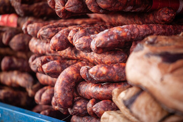 Fototapeta premium Close-up of cajna kobasica sausages stacked for sale on a Serbian market stand, showing the dense texture of this traditional smoked cured pork product commonly known as tea sausage.