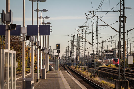 Platform view at Troisdorf train station in Germany, with dense railway wires, signals and a Cologne Koln S-Bahn train visible on the right. The scene highlights commuter rail infrastructure in NRW.