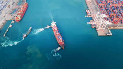 Obraz premium large container ship assisted by tugboats near a busy commercial port and terminal. Global maritime trade logistics, freight transport, and energy commodity supply chain concept.