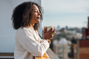 Fototapeta premium Beautiful woman drinking a cup of tea while relaxing on her balcony at home