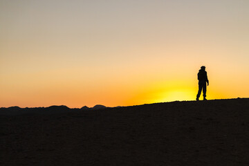 Fototapeta premium Silhouette of traveler walking across desert ridge at sunset in Egypt with mountains on horizon