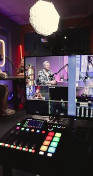 Close up modern podcast studio with hosts recording interview, with professional lighting, microphones, live production monitor displays multiple cameras. Media production in creative broadcast space