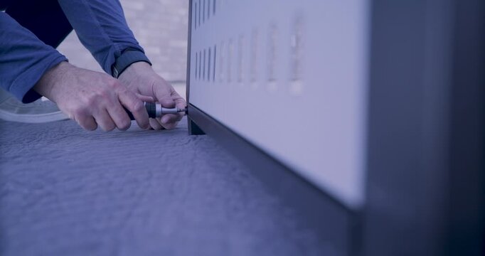 Rack focus of man quickly tightening screws on bottom of grill with screwdriver 
