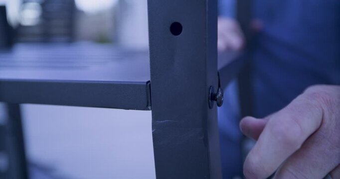 Grown man hand screwing a screw into metal bar of structure - closeup