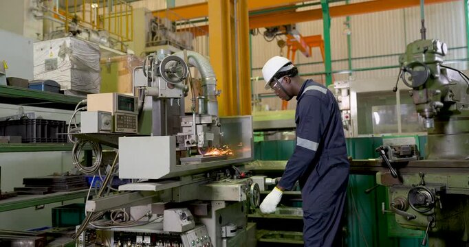 African adult male technician stands beside production machine in slow motion, observing industrial equipment during manufacturing workflow, supporting safety, process control, automation monitoring.