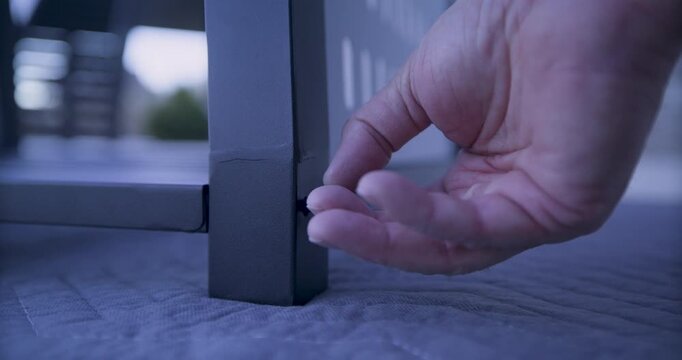 Adult hand screwing long screw in the bottom of metal leg of grill - closeup