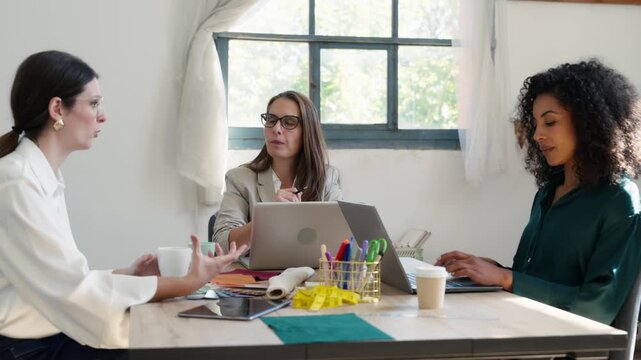 Video of group of fashion designers choosing fabrics while creating new designs on the laptops in a coworking place