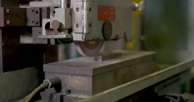 closeup of grinding wheel cutting metal block with bright spark in workshop, precision machining process, industrial safety control and monitored production operation in motion