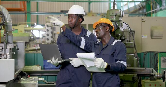 African adult male engineers review laptop data and printed document beside industrial machine, discussing production planning, process optimization and real time monitoring in workshop