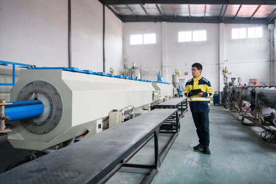 Worker inspecting large extrusion machine equipment in factory workshop