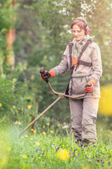 Woman mows grass in a green lawn using a lawn mower trimmer on a sunny day in a residential area