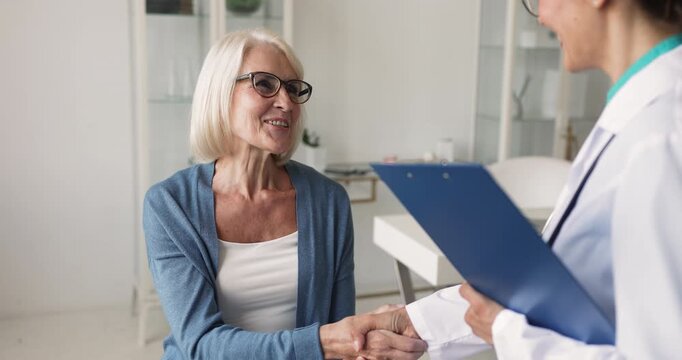 Smiling middle age woman patient talk to female doctor during medical consultation in clinic, finish visit with handshake, gesture of respect, trust, satisfaction with professional health care service