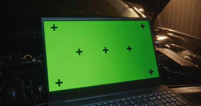 Laptop Computer With Green Screen Interface and Tracking Markers For Screen Replacement. Device Integrated Into Car Maintenance Scene, Positioned Next to Engine Blocks in Modern Service Center.