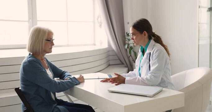 Female doctor in white coat sits at desk in clinic office, gives heath recommendations, explains treatment options, shaking hands with woman patient, ending medical consultation. Healthcare, trust