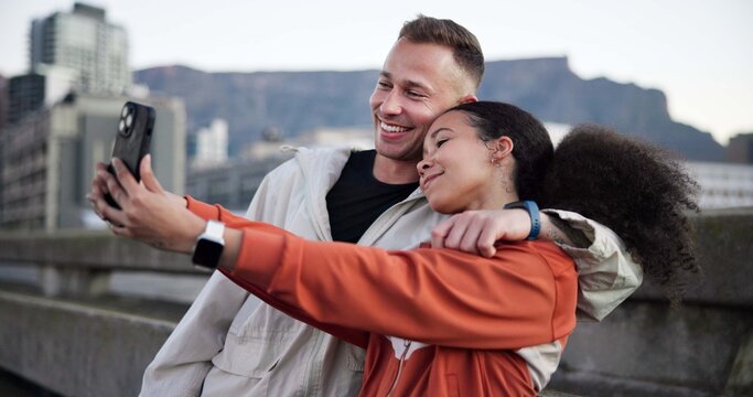 Happy couple, fitness and phone with selfie in city with hug, love or bonding with break on bridge. People, runner and photography with mobile app, smile and rest for interracial relationship in town