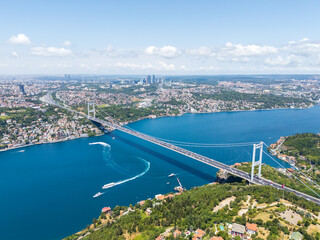 Obraz premium Istanbul, Turkey. The 15 July Martyrs Bridge (Bosphorus Bridge) connecting Ortakoy (Europe) and Beylerbeyi (Asia), with ships sailing the Bosphorus strait on a summer midday. Aerial view