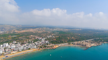 Fototapeta premium Kizkalesi, Mersin, Turkey. Breathtaking panoramic drone view from Maiden Castle island showing surrounding sea, city beaches and majestic Taurus mountains.. Aerial View