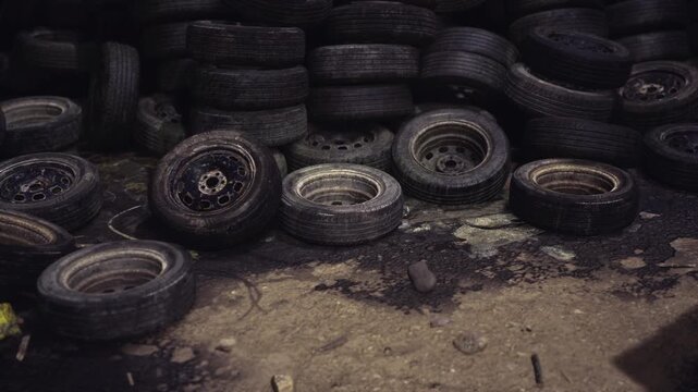 Dilapidated tire storage area. Discarded tires stacked amid muddy surroundings. Neglected industrial tire dump at sunset with scattered rims and debris