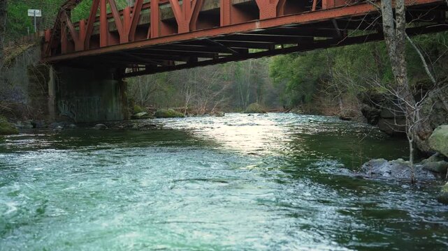 Rushing creek flowing underneath an old bridge within Lassen National Forest during a light breeze