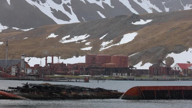 Snow falls over Grytviken&rsquo;s rusting whaling station ruins and shipwreck in South Georgia, with dark harbor water and patchy snow on the hills.