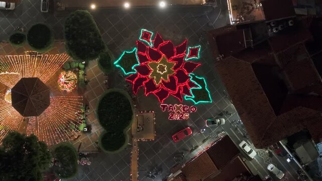 Top-down aerial view of the giant Christmas flower in Taxco at night, illuminated with the year 2025 in the main cobblestone square, Guerrero, Mexico