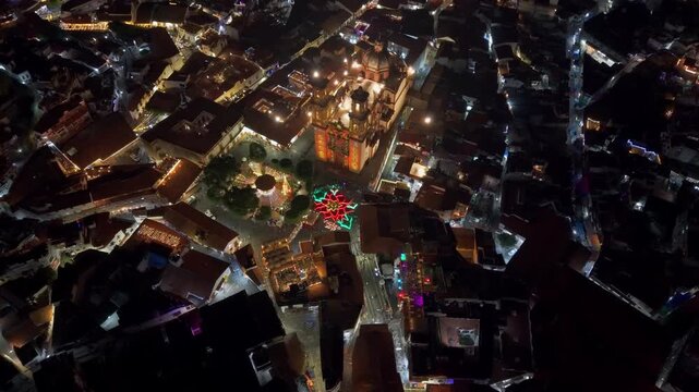 Aerial view establishing tilt up of the Santa Prisca temple in Taxco at night with the giant illuminated poinsettia and interconnected stone streets, Guerrero, Mexico