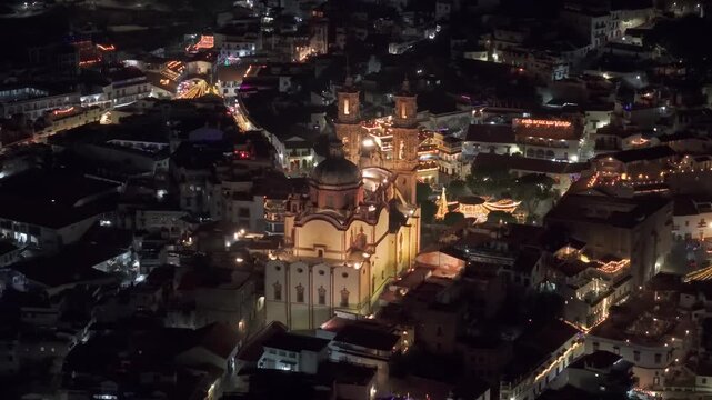 Establishing cinematic aerial view of the parish of Santa Prisca in Taxco at night, with illuminated and interconnected streets, Guerrero, Mexico. Magical town.