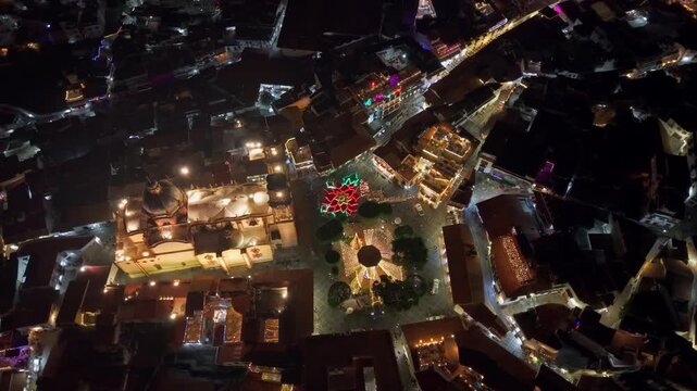 Aerial view establishing of the Santa Prisca temple with the poinsettia at night and illuminated, interconnected streets, colonial architecture, state of Guerrero, Mexico