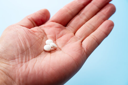 Close-up of human palm holding white pills or supplements on blue background