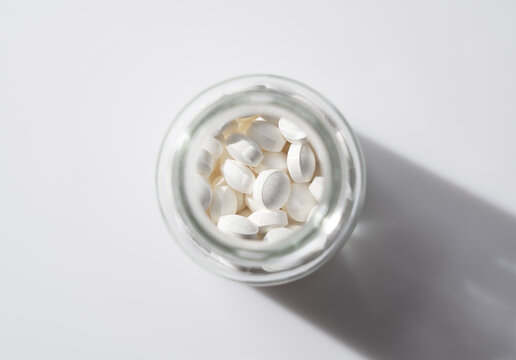 Overhead view of white medical pills or supplements in a glass bottle on white background